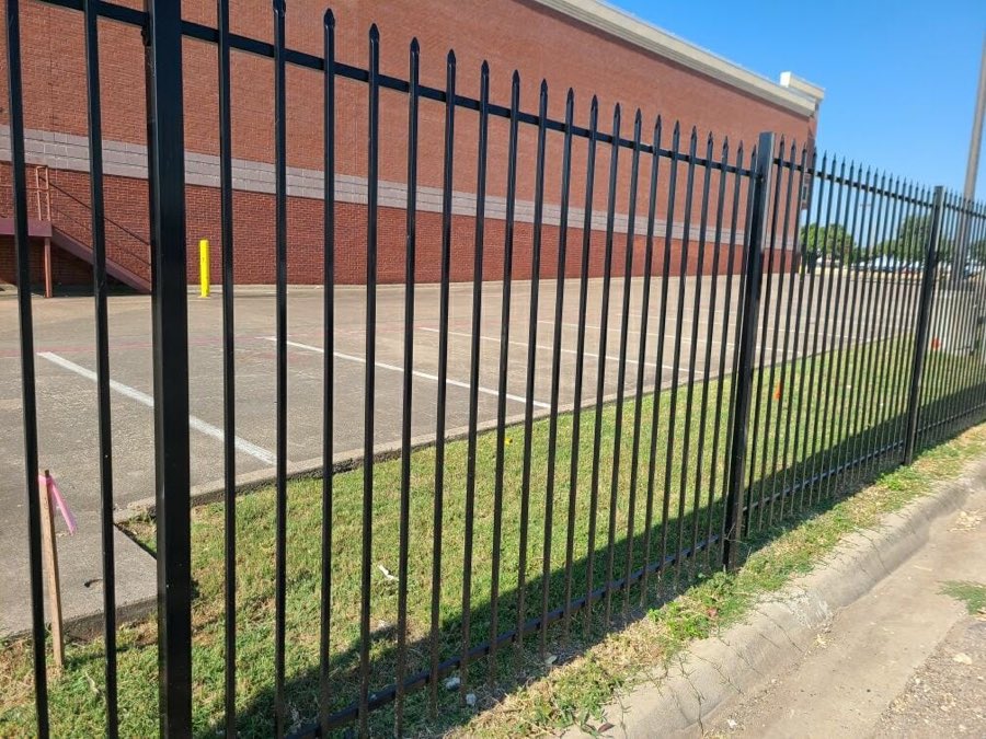 Six foot black steel picket fence along a commercial parking lot